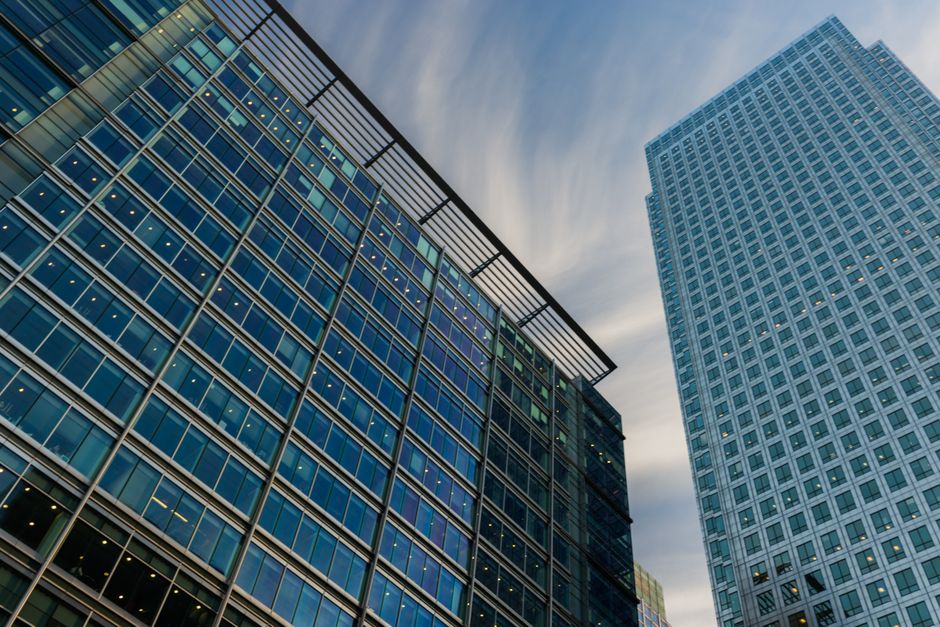 Upward perspective of modern glass skyscrapers with a blue sky background, representing corporate headquarters and public market scale.