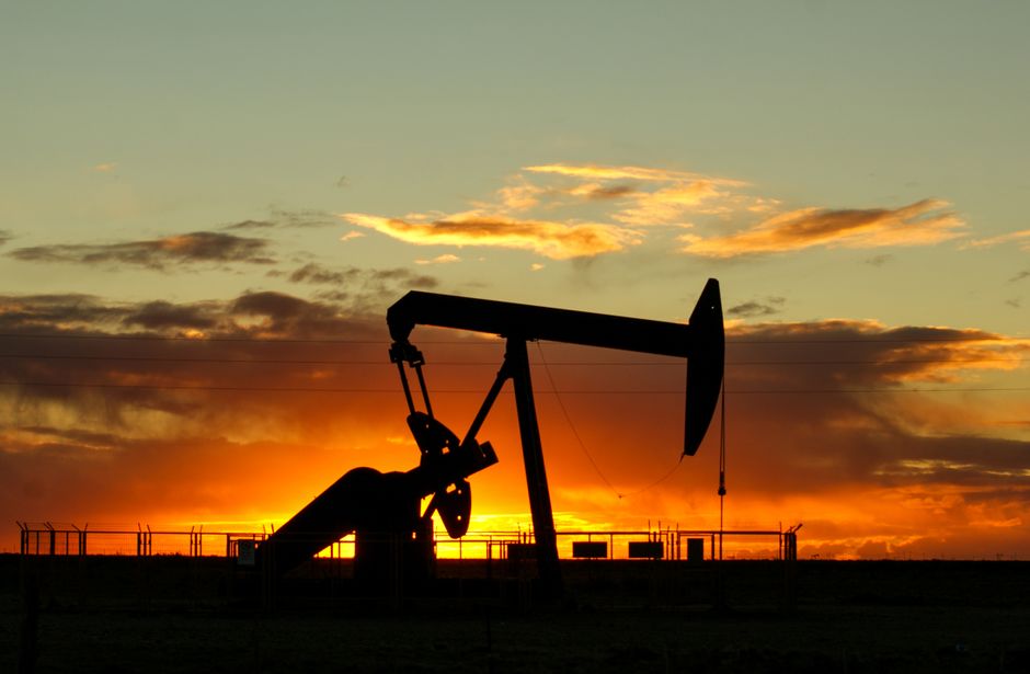 Silhouette of an oil pump jack against a vibrant sunset sky.
