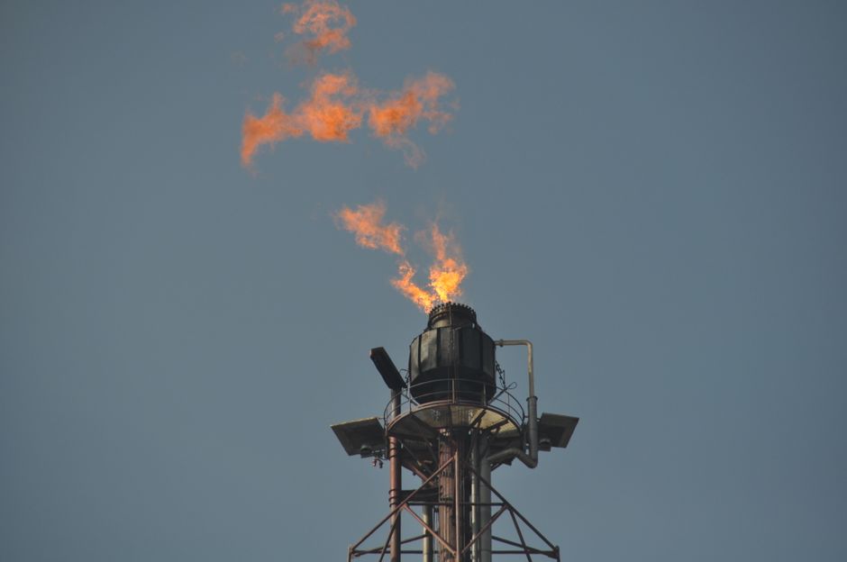 Flare stack releasing flames at an industrial petrochemical site.