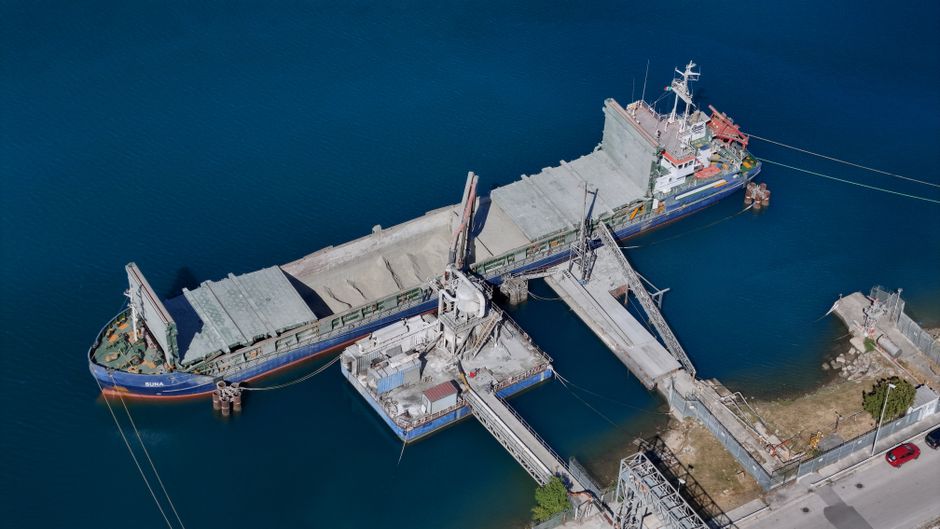 A cargo ship docked at an industrial loading facility, illustrating the maritime infrastructure exposed to geopolitical risk.
