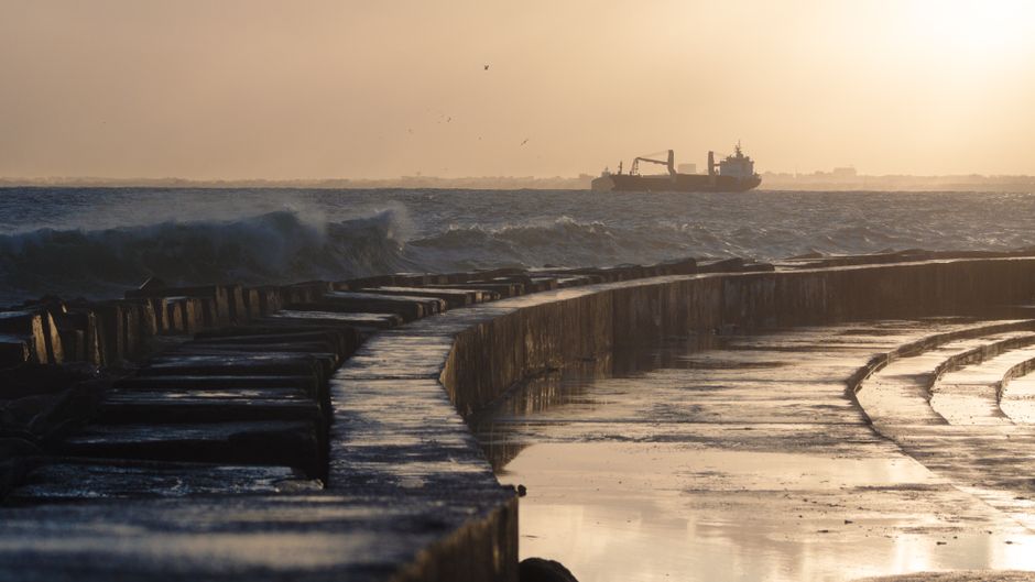 Freighter ship sailing across the ocean at sunrise, representing the maritime shipping routes disrupted by the Strait of Hormuz crisis.
