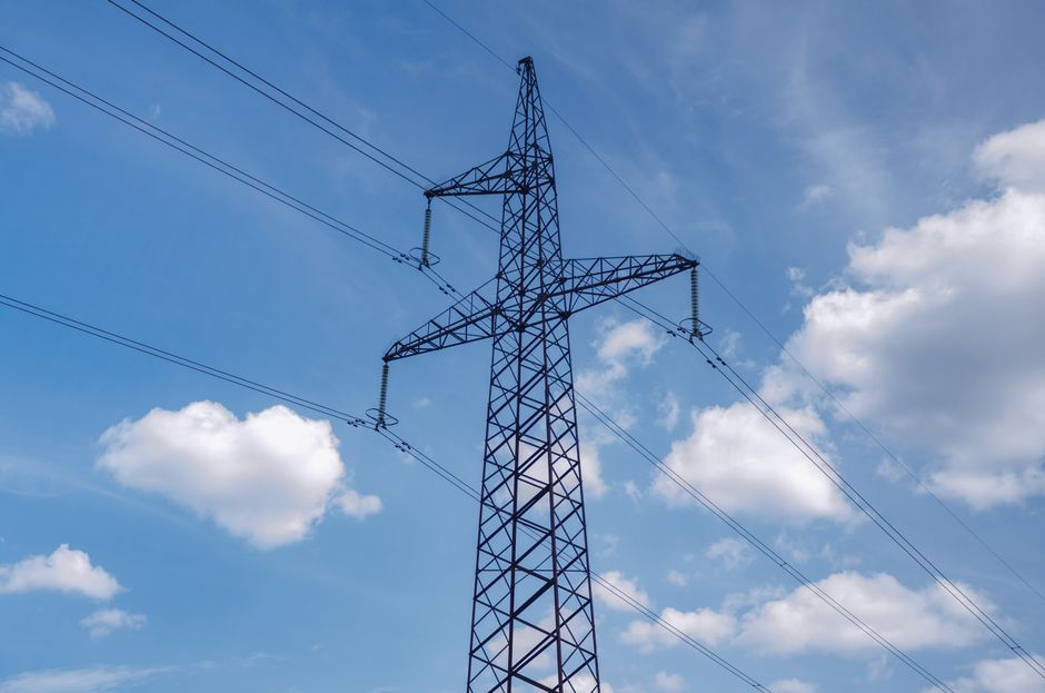 High-voltage transmission tower against a blue sky with scattered clouds.