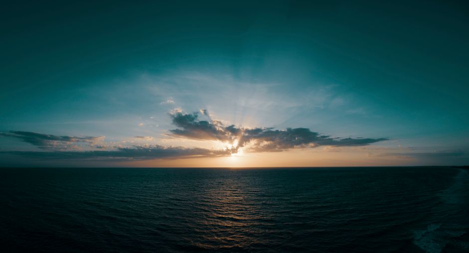 Dramatic sunset over calm ocean waters with dark clouds on the horizon, evoking the Strait of Hormuz maritime backdrop.