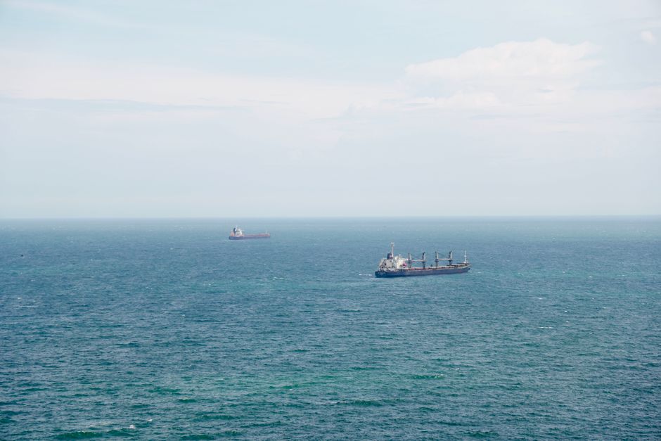 Two cargo ships navigating the expansive ocean under clear blue skies, illustrating maritime shipping through contested waters.