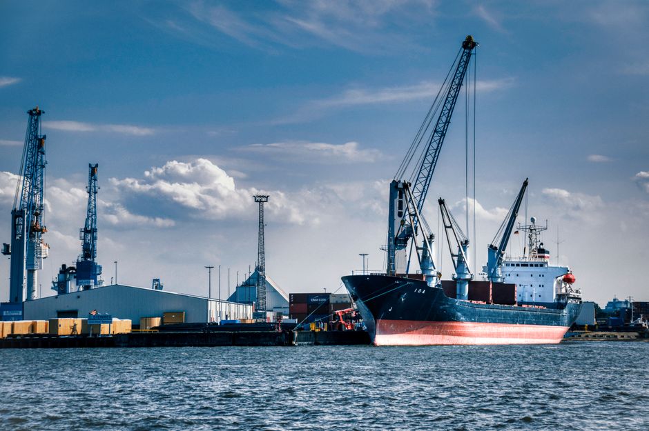 A cargo ship loaded with containers at a busy harbor under a clear blue sky.