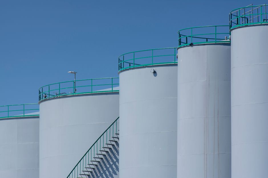 Large industrial petroleum storage tanks with green railings standing against a clear blue sky.