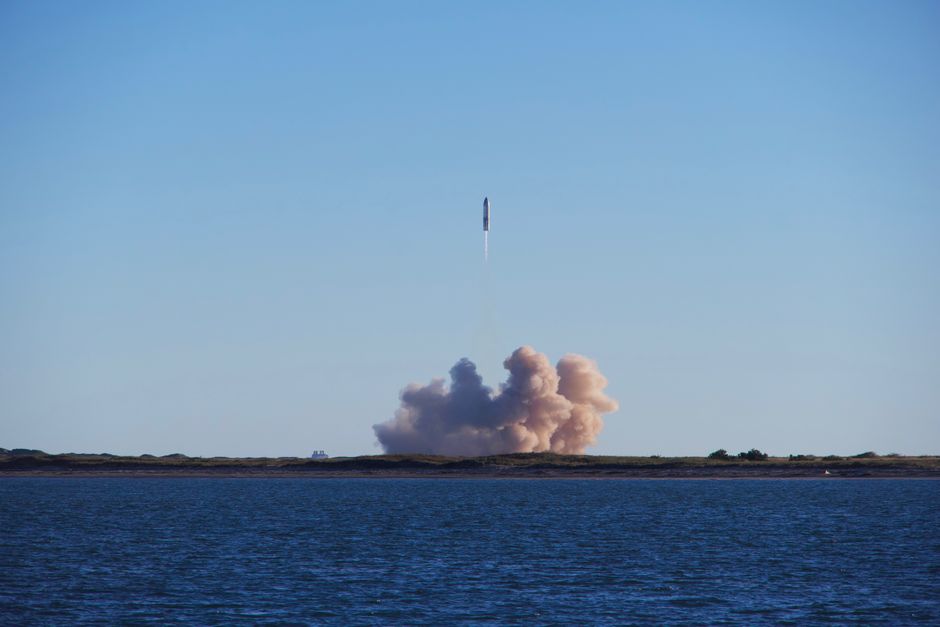 A rocket lifting off with a column of exhaust against a blue sky, viewed from a distance.