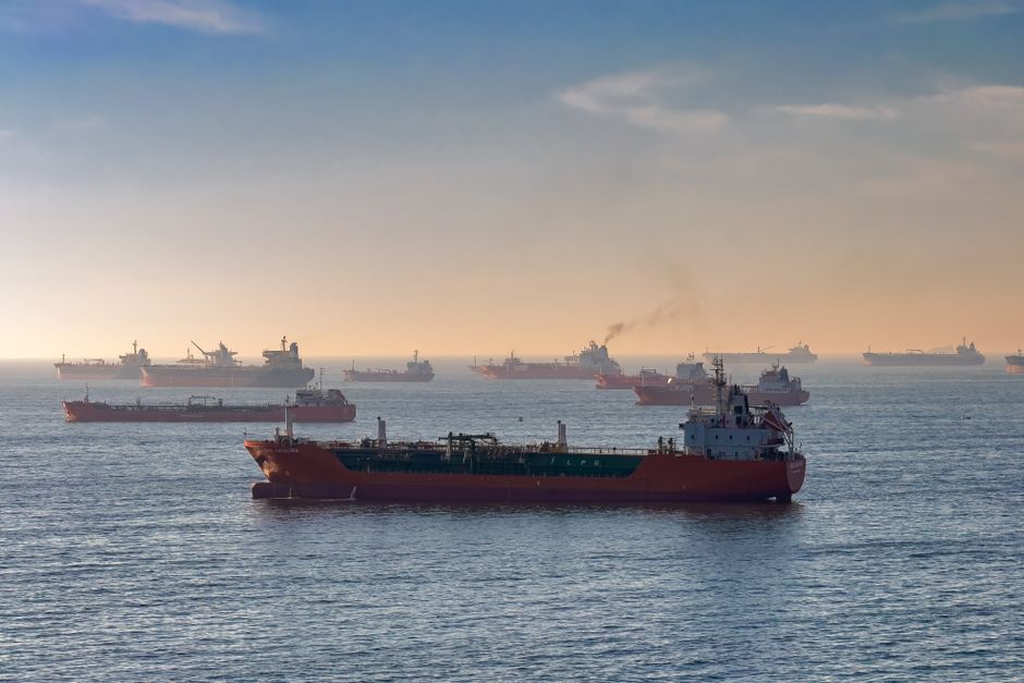 Oil tankers and cargo ships navigate a narrow strait at sunset, reflecting global energy trade routes.