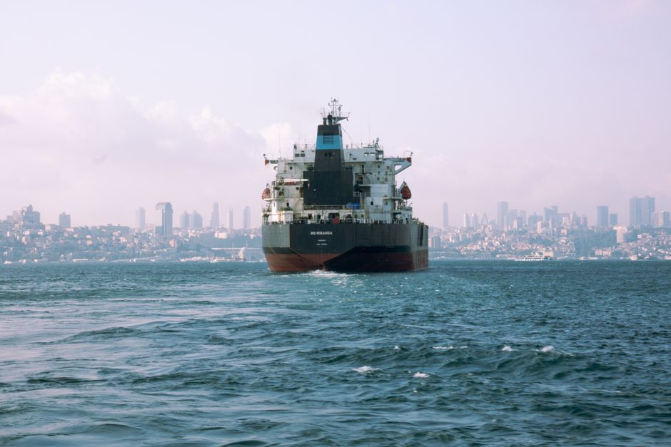 Cargo ship transiting a narrow strait near a city shoreline