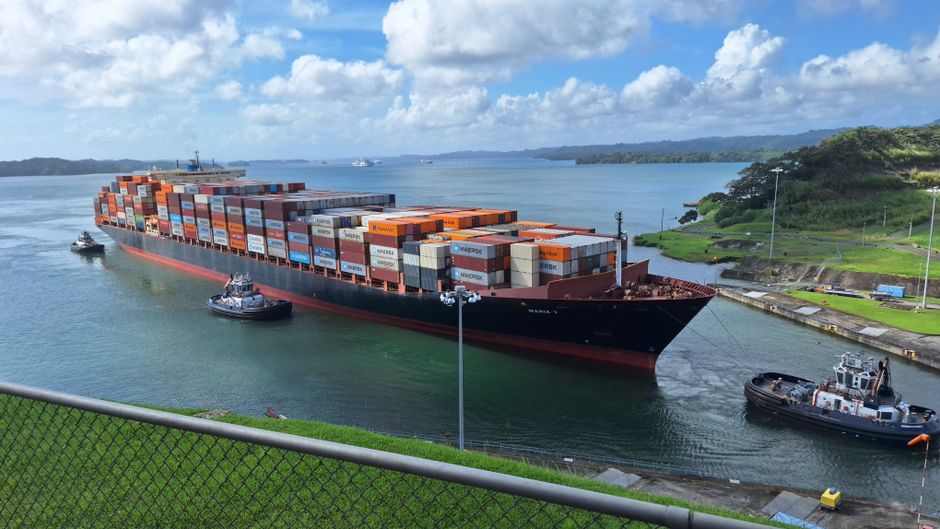 Large container ship maneuvered by tugboats through a narrow canal, representing constrained maritime routes carrying energy supplies.