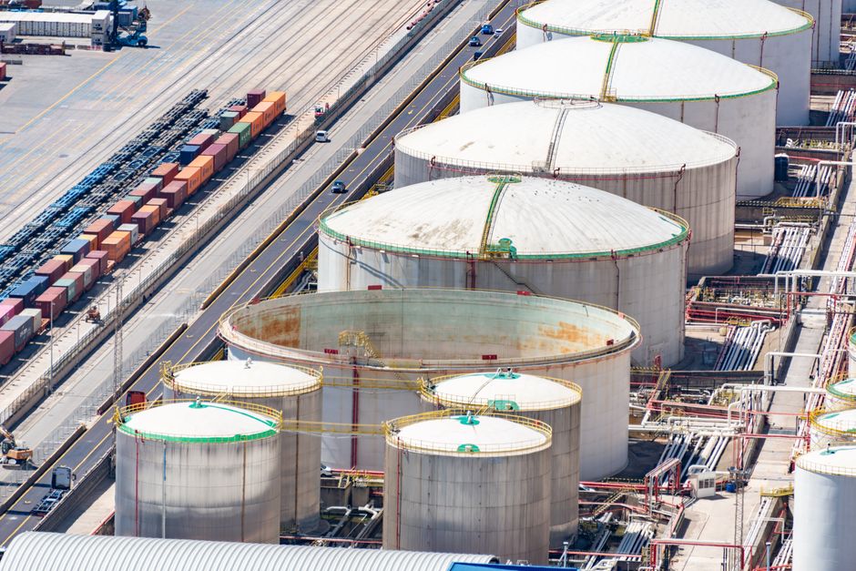 Aerial view of large cylindrical oil storage tanks in an industrial district with adjacent railway tracks.