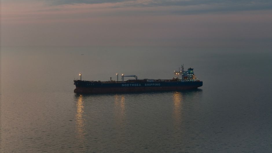 Oil tanker sailing on calm open waters at twilight, silhouetted against a muted sunset sky.
