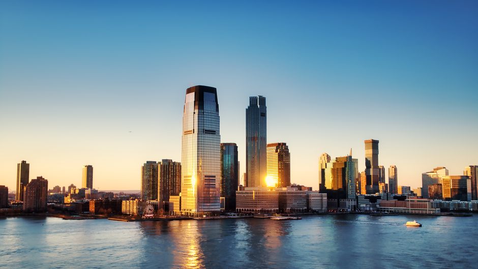 A sunrise view over the New York City skyline with golden light reflecting off skyscrapers across the water.