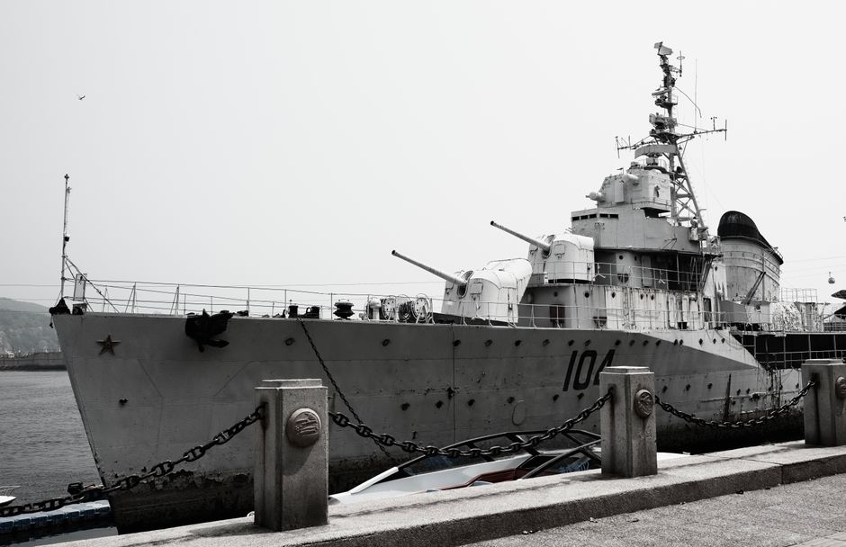 A large naval destroyer ship docked at a harbor under a gray sky.
