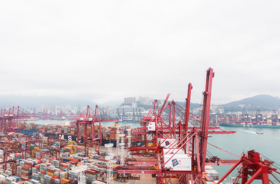 Container cranes and stacked cargo at a commercial harbor, illustrating the supply chain linking geopolitical shocks to corporate margins.