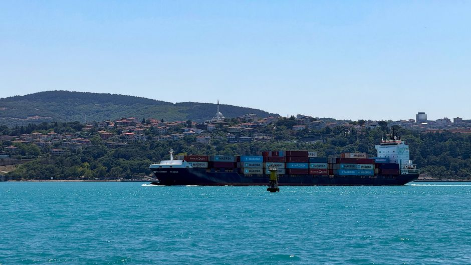 A container ship navigates a narrow strait as geopolitical tensions raise risks for global shipping routes.