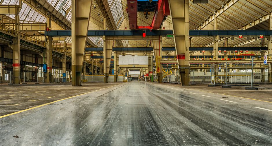 Wide view of an industrial warehouse with cranes and metal structures, evoking the physical buildout behind AI infrastructure.