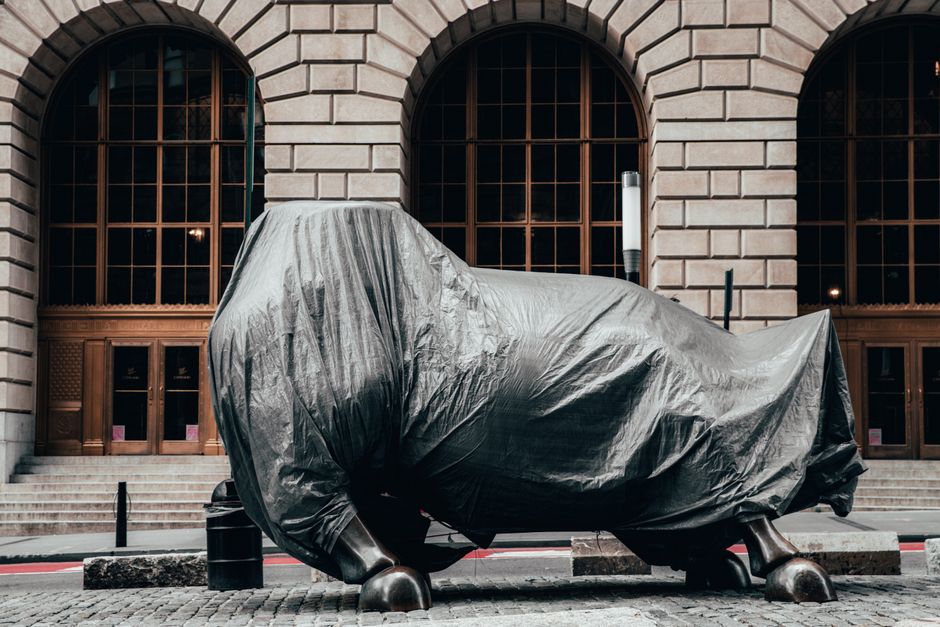 Covered Charging Bull statue on a Wall Street sidewalk, symbolizing market volatility and uncertainty.