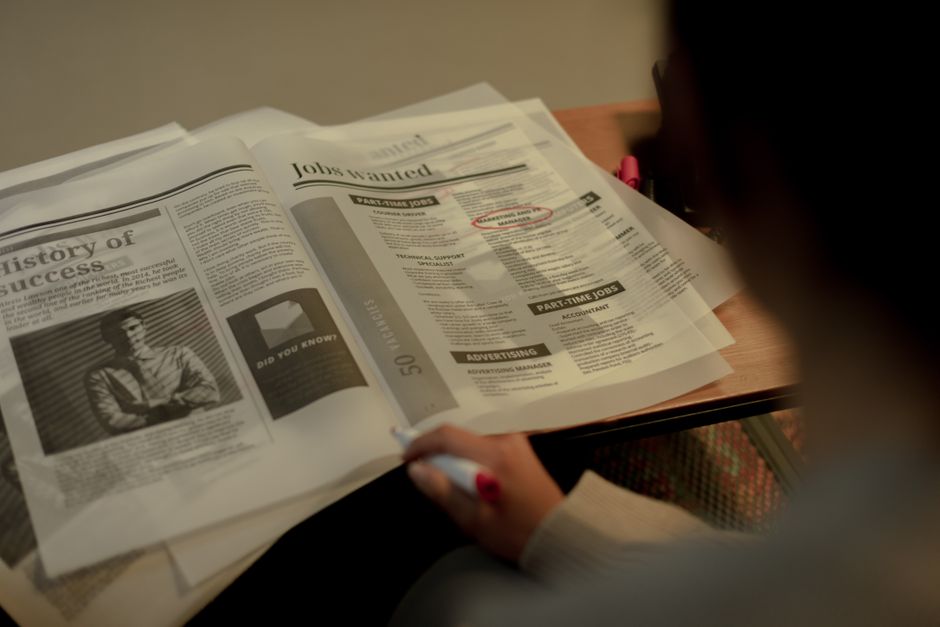 Person reviewing job listings in a newspaper, holding a pink marker for highlighting job ads