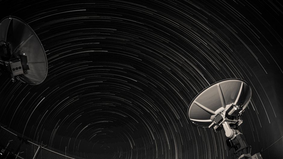 Satellite dishes under star trails in a long-exposure night sky photograph