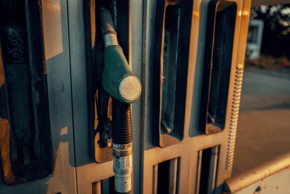 A gasoline pump nozzle shown in silhouette against a sunset sky.