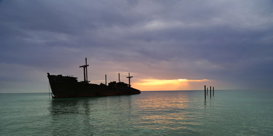 Silhouette of a large ship stranded at sunset on the coast of Kish Island in the Persian Gulf, under a dramatic sky.