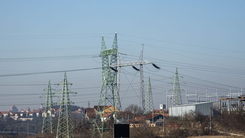 High-voltage transmission towers and power lines near an urban area, representing the grid constraints around data-center expansion.
