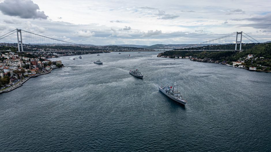 Military ships moving through a strategic maritime waterway amid elevated geopolitical risk.