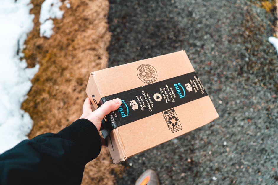 A person holding an Amazon Prime package on an urban sidewalk