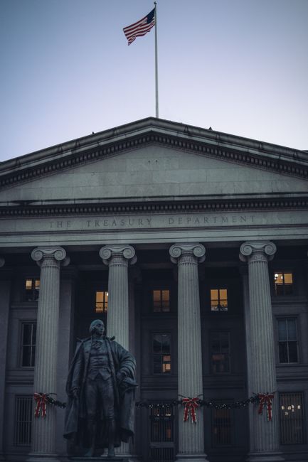 View of the US Treasury Department building facade with columns and American flag at dusk.