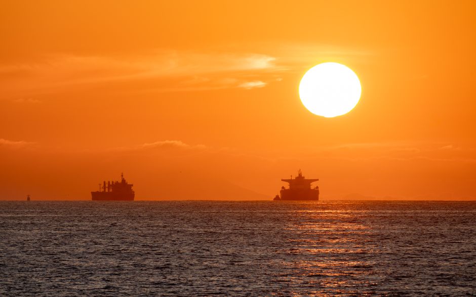 Oil tankers silhouetted against a vibrant sunset over the ocean, illustrating seaborne crude transport.