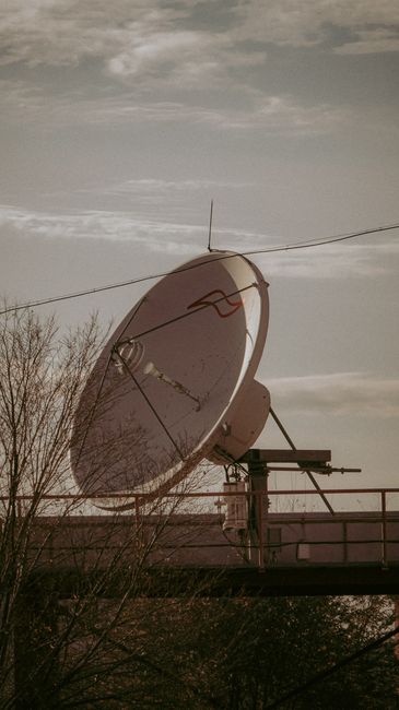 Large satellite dish against a cloudy sky, symbolizing communication and technology.