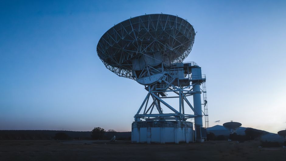 A large radio telescope dish under a twilight sky, positioned to receive cosmic signals.