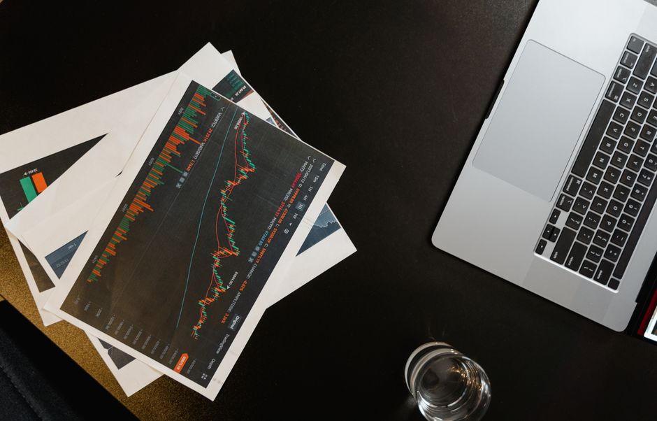 Capital-markets documents and charts beside a laptop, representing underwriting and public offerings.