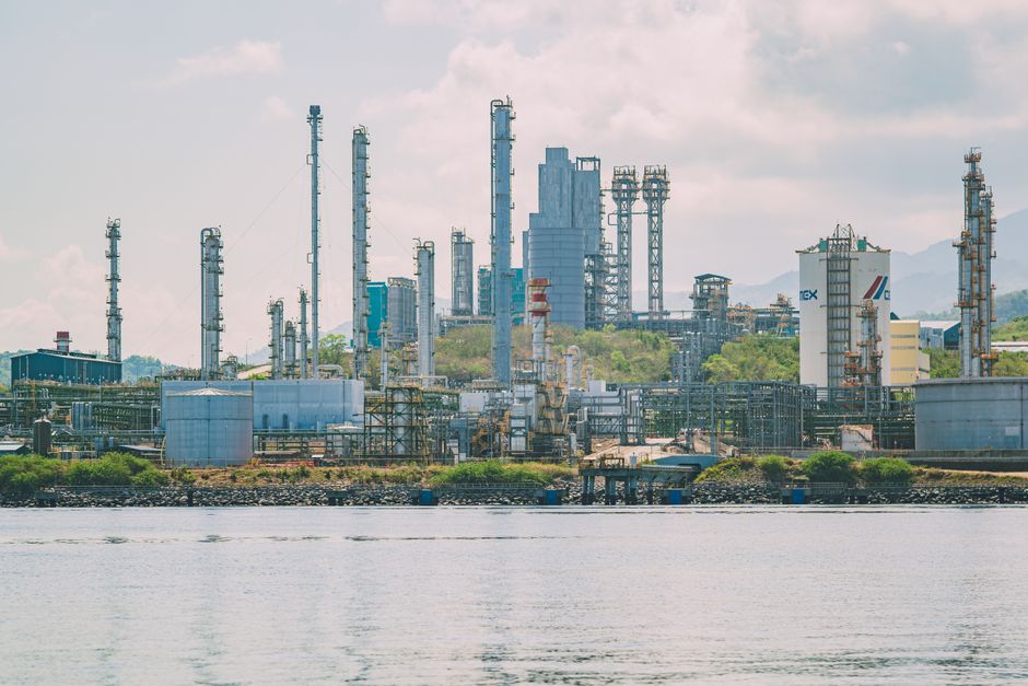 A large industrial refinery complex with tall chimneys by the waterfront.