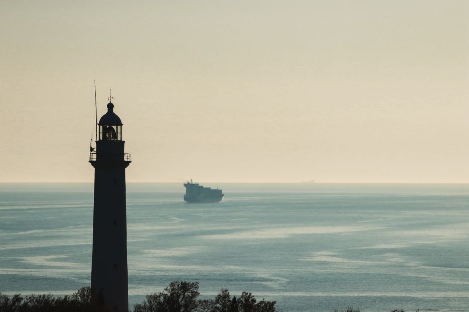 A lighthouse on a strait coastline with a ship on the horizon