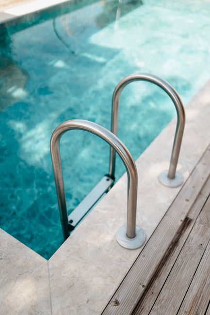 A stainless-steel ladder rises from the deep blue water of a backyard swimming pool.