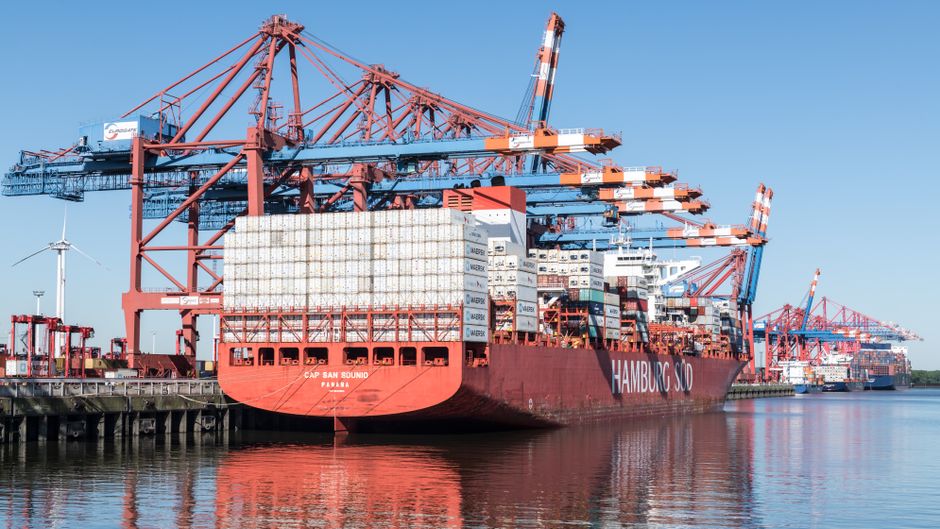 Large container ship docked at a port with cargo cranes in view