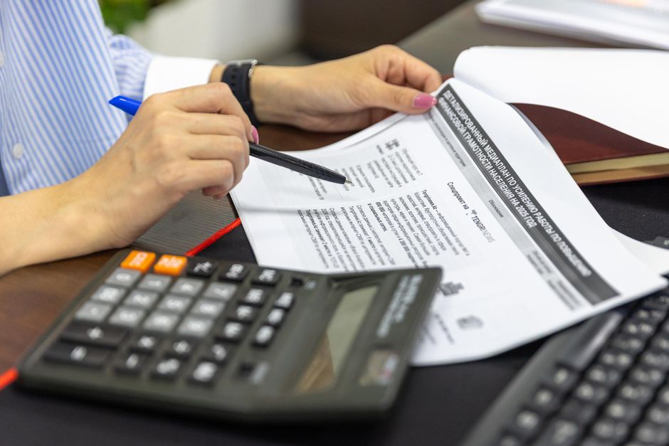 Person's hands using a calculator and pen over printed financial statements and documents