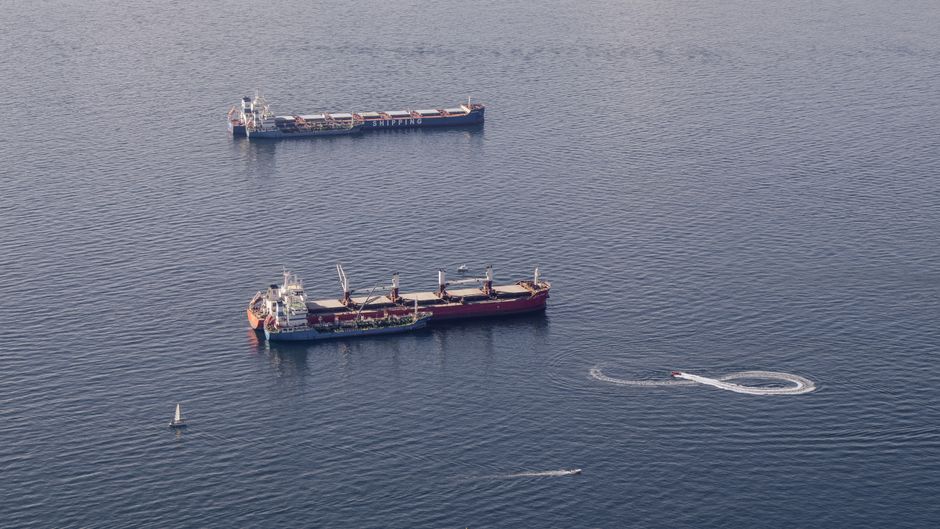 Aerial view of two cargo ships transiting crowded waterways, with smaller boats nearby.