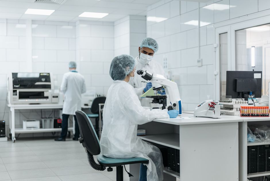 Two scientists in lab coats examining samples under microscopes in a research laboratory.