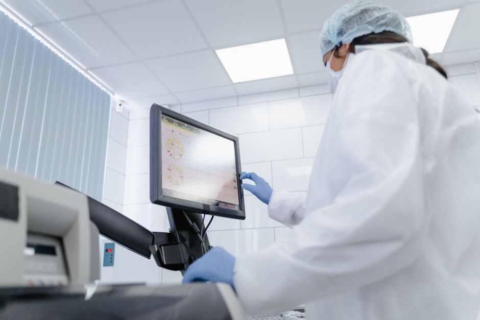 Scientist in a white lab coat operating a touchscreen monitor in a modern pharmaceutical research laboratory