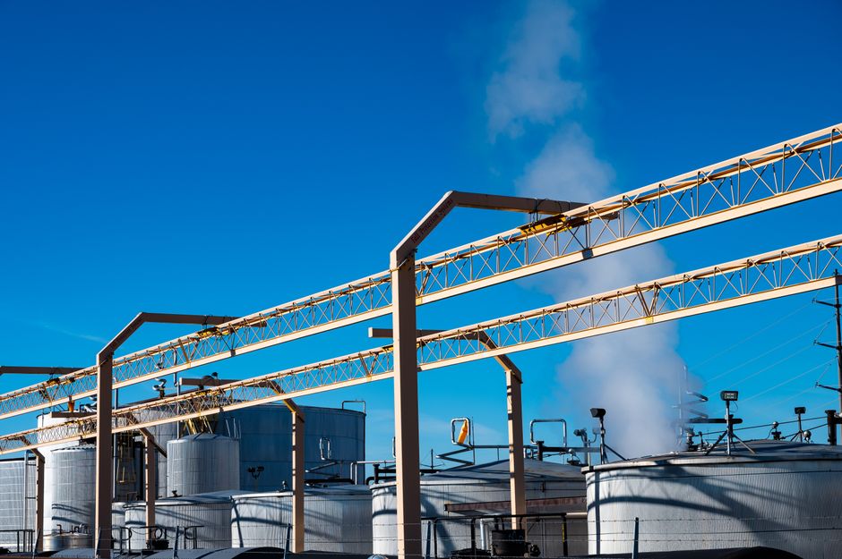Wide view of an industrial oil refinery with storage tanks and smoke against a clear sky, illustrating the energy infrastructure at stake in the Strait of Hormuz crisis.
