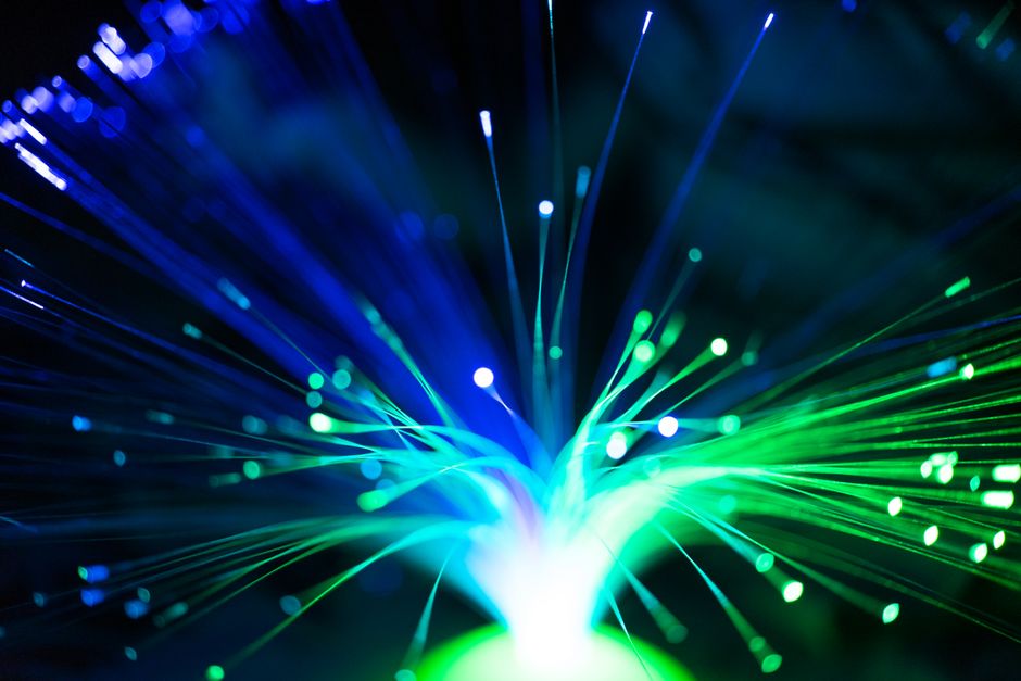 Close-up of illuminated fiber optic cables in blue and green, representing the network infrastructure powering cloud computing and AI services.