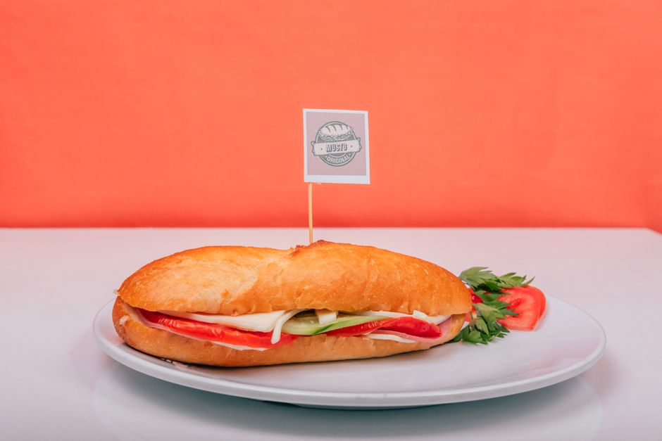Fresh sub sandwich filled with vegetables on a white plate against an orange background