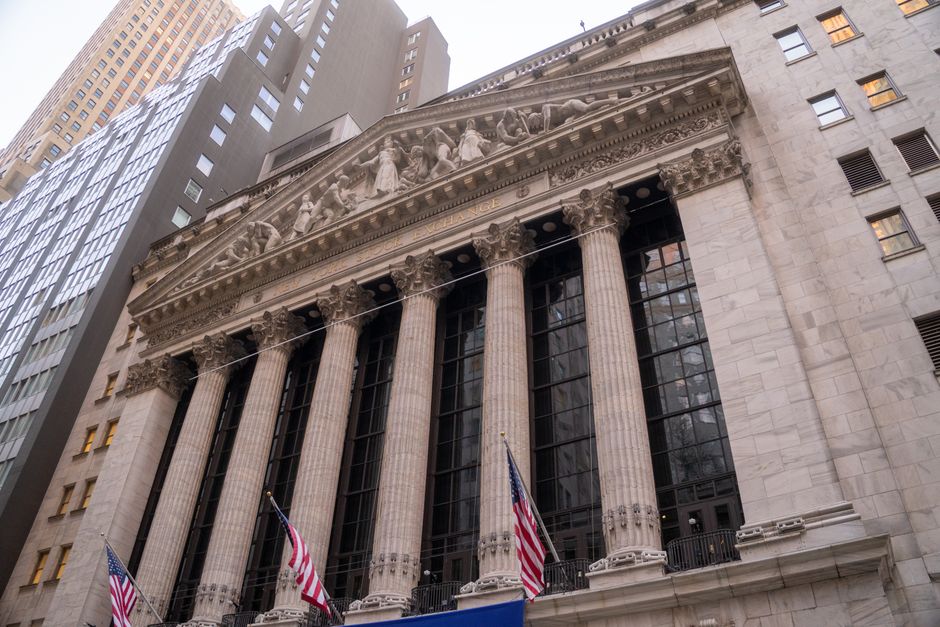 The New York Stock Exchange building facade with American flags displayed on Wall Street.