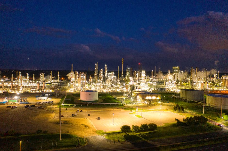 An illuminated oil refinery represents the energy-supply shock that can feed into inflation, interest rates, and markets.