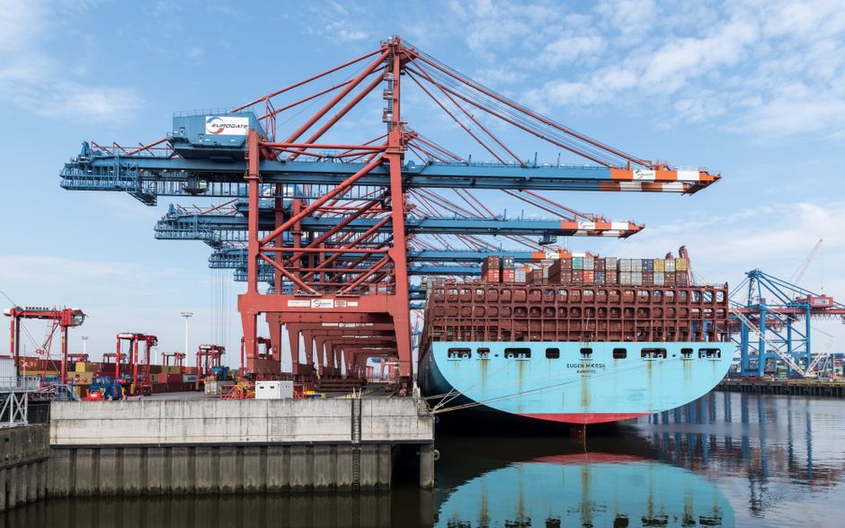 Container ship being loaded at a port terminal with gantry cranes, representing global trade flows through maritime chokepoints.