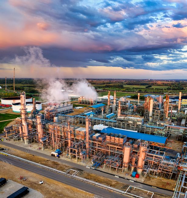 Aerial view of an oil refinery at sunset, with industrial processing structures and storage tanks.