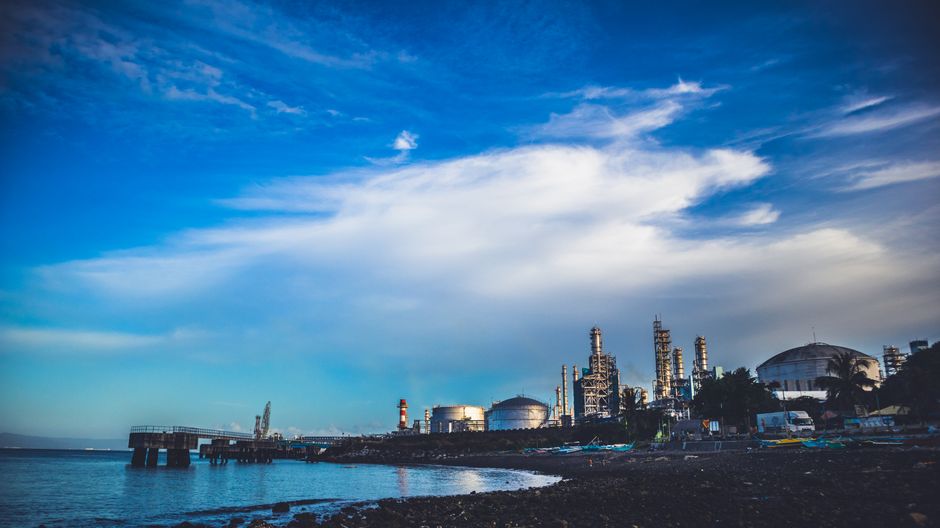 Industrial oil and gas facilities by the sea under a dramatic cloudy sky